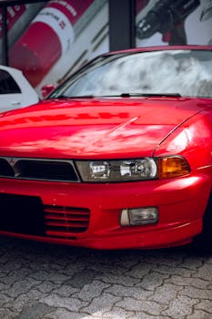 Close-up of a bright red vintage sports car parked outdoors on a cobblestone street.